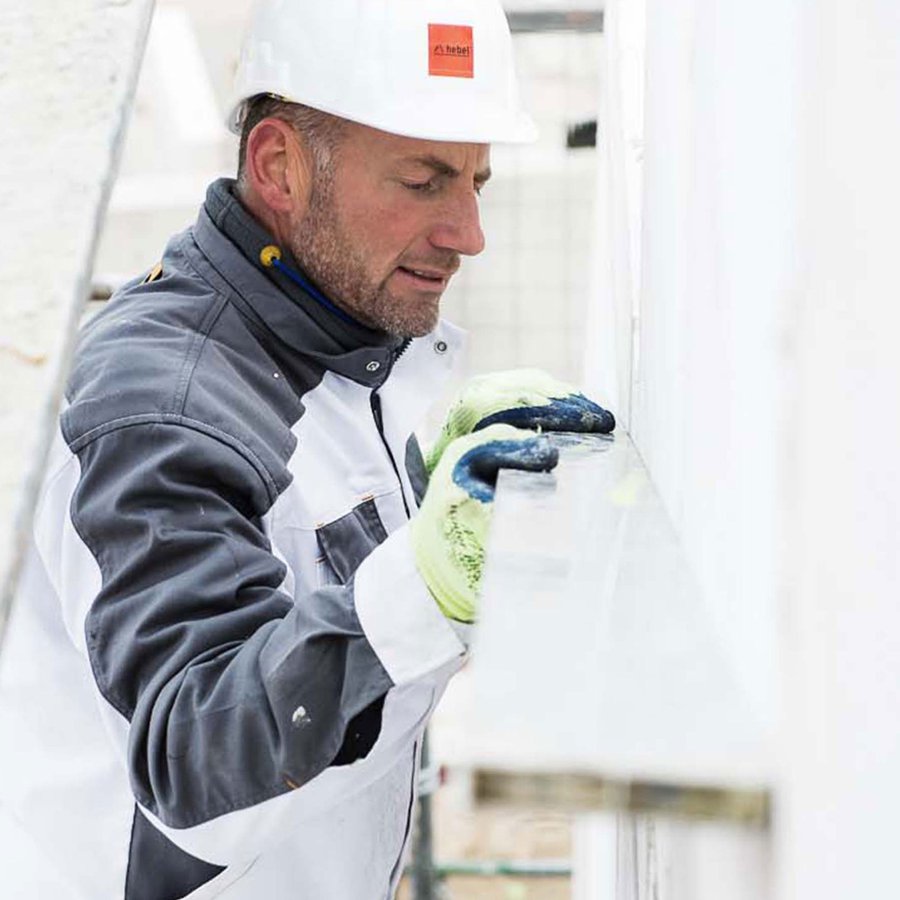 Ein Arbeiter auf der Baustelle prüft die Ausrichtung einer Gebäudehülle aus massivem Porenbeton