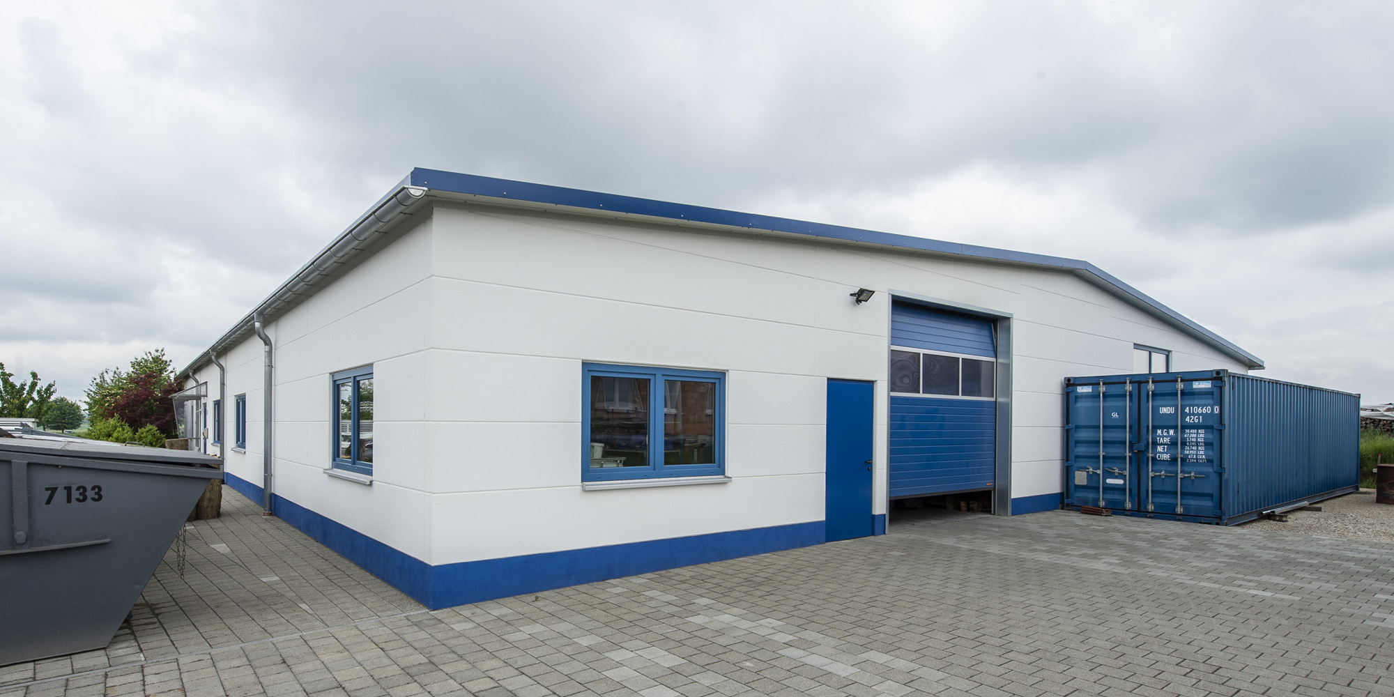 Ein Depot für Lagerware mit blau-weißer Fassade als Erweiterung einer bestehenden Halle