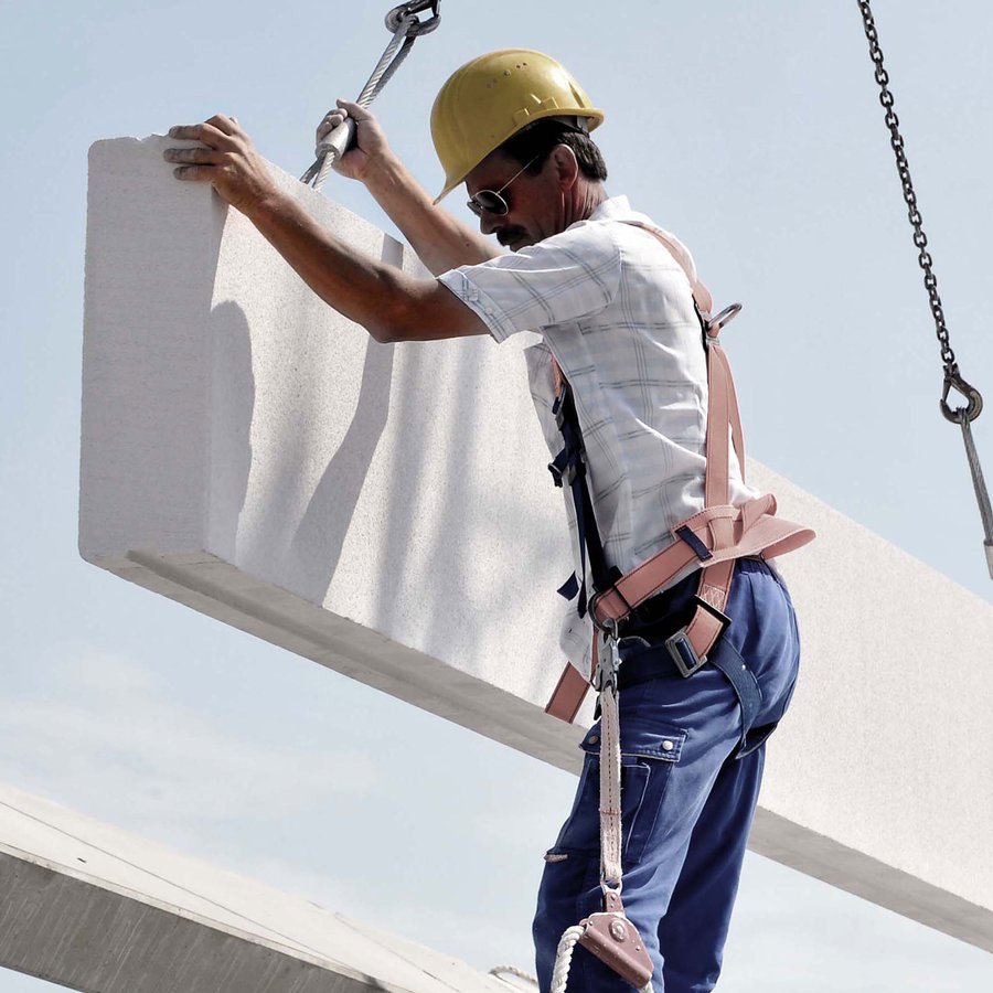 Ein Arbeiter auf der Baustelle justiert ein großes Montagebauteil an einer neuen Gewerbehalle