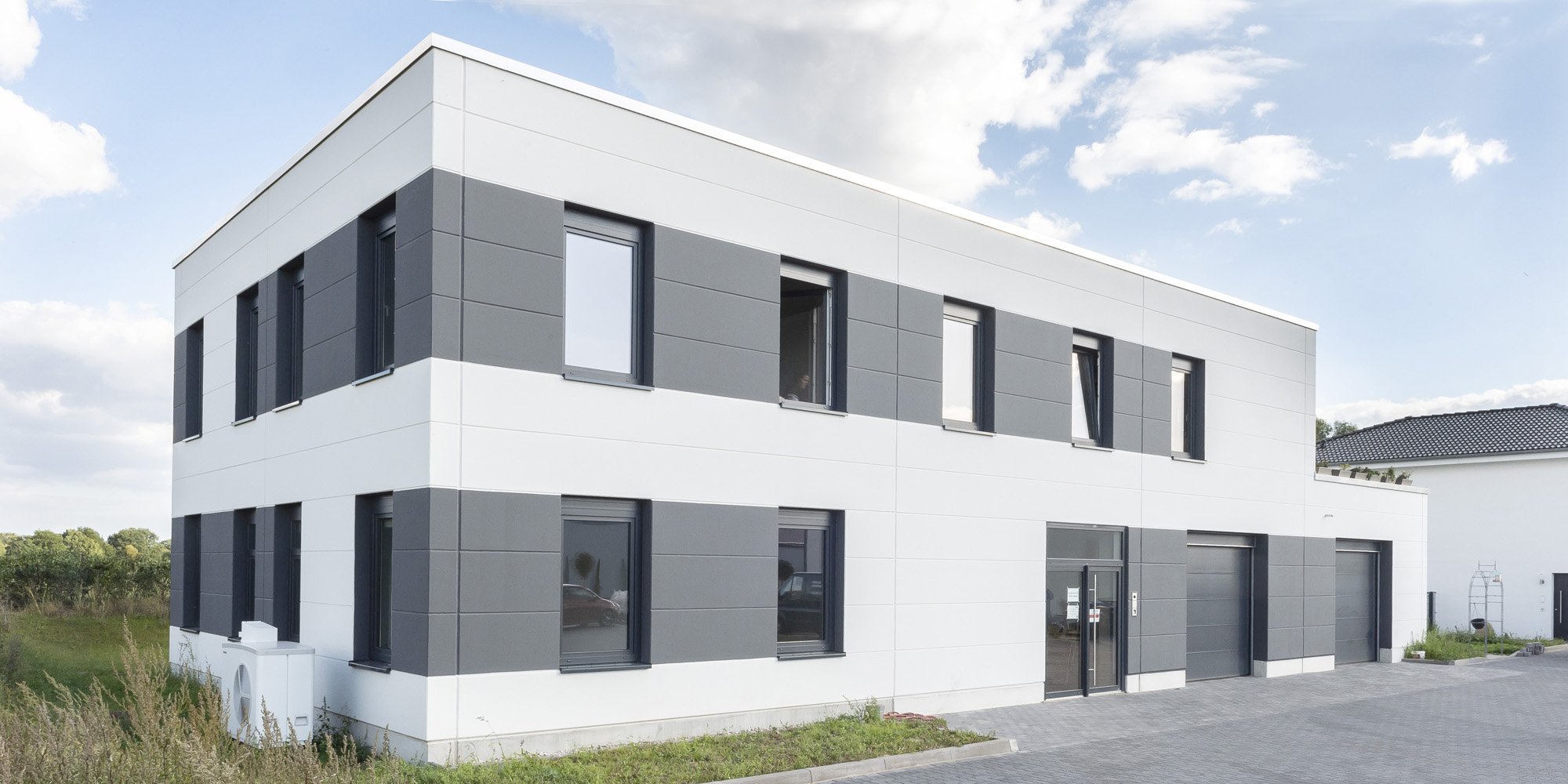 Kombinierte Werkstatt, Büro, Showroom und Betriebswohnung mit weißer und grauer Fassade aus Porenbeton