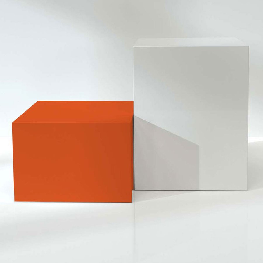 Ein kleiner orangener Klotz steht neben einem großen weißen Klotz auf spiegelnder Oberfläche